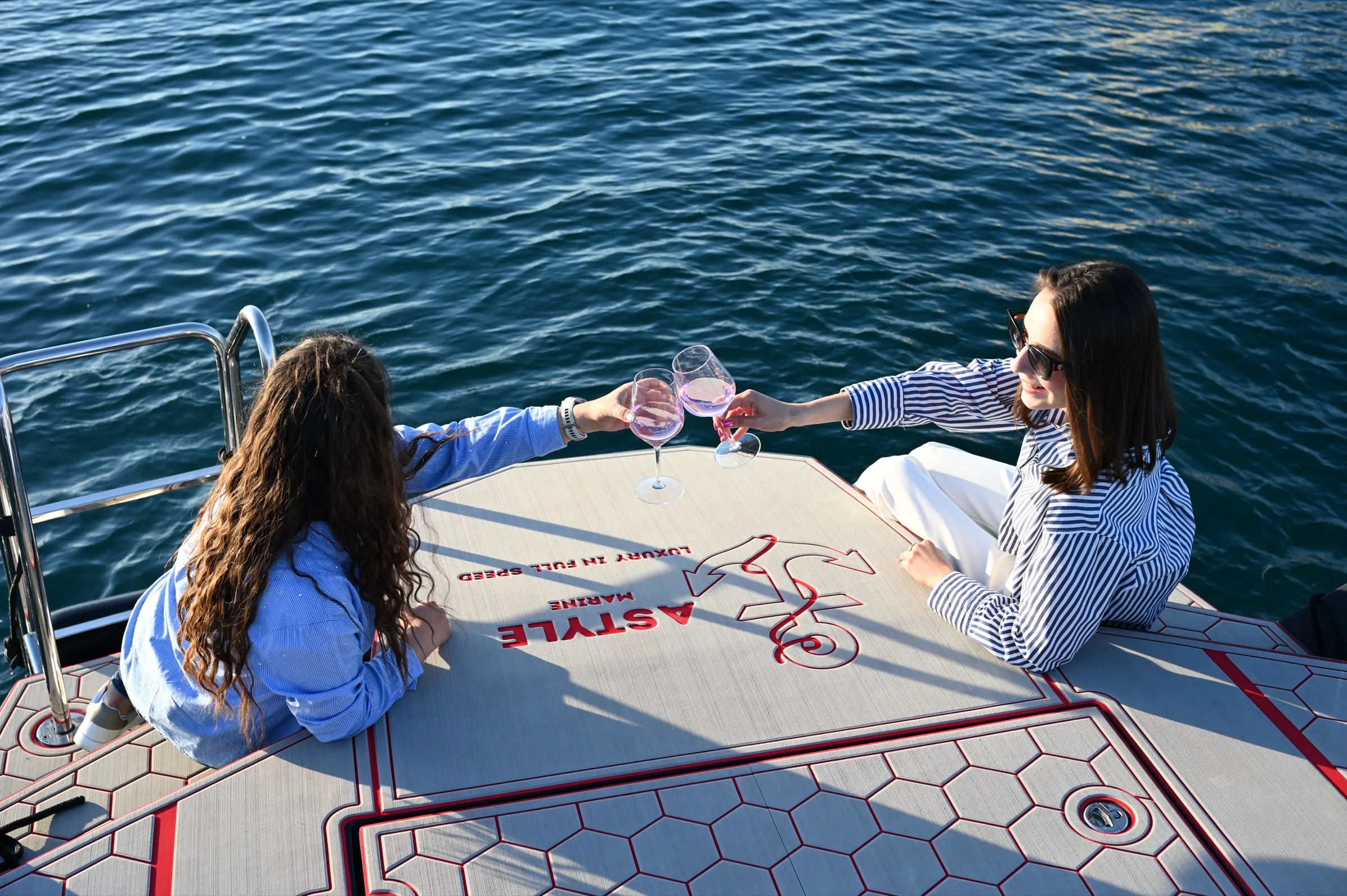 Dvije gošće nazdravljaju čašama rosé vina preko pramca s logotipom Astyle Marine, ispod njih tamnoplavo more